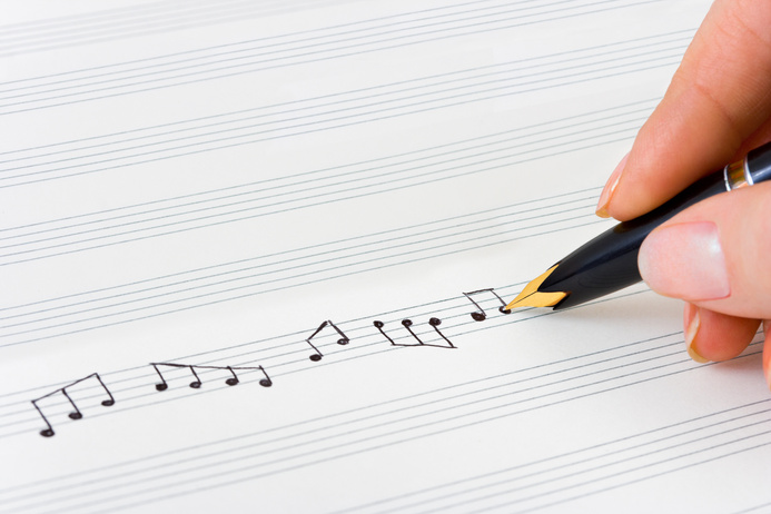 Hand using pencil to write musical notes on sheet music